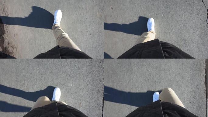 在阳光明媚的日子里，穿着白色运动鞋的男人穿着牛仔裤走在人行道上。视点视频，第一人称