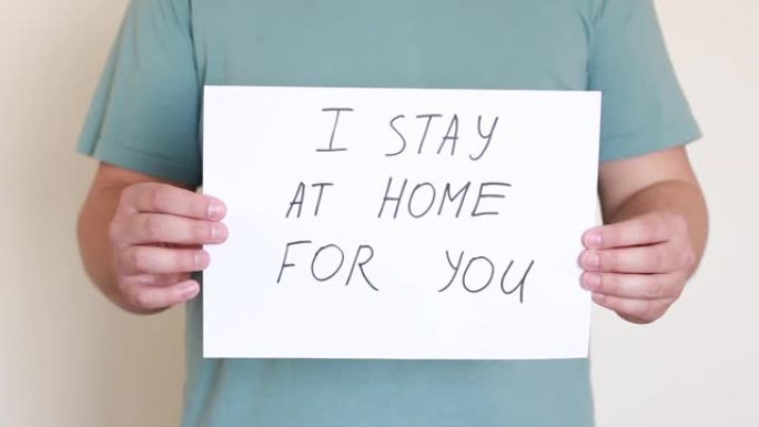 在冠状病毒流行期间，男人拿着一份写着 “我为你呆在家里” 的论文
