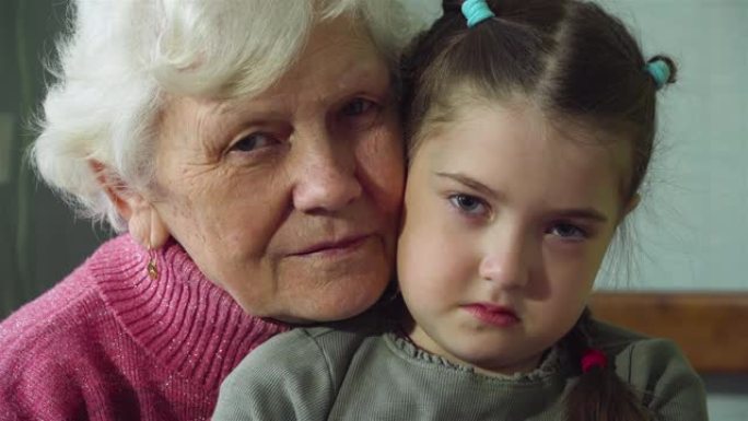 老妇人奶奶的肖像带着悲伤的孙女拥抱，看着房间里的相机。两代人之间的温暖关系