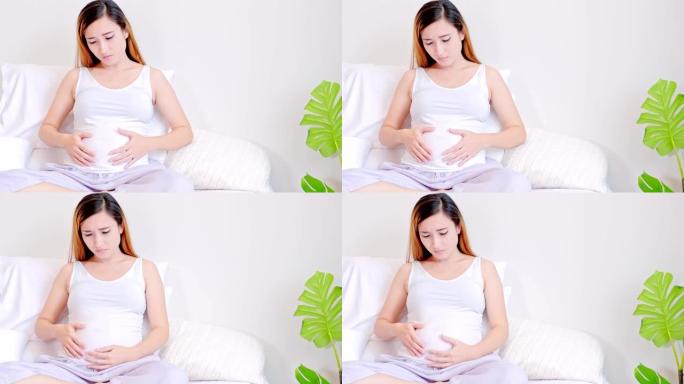 孕妇在床上抚摸着自己的肚子，心情很担心。亚洲的女人。年轻父母的概念。