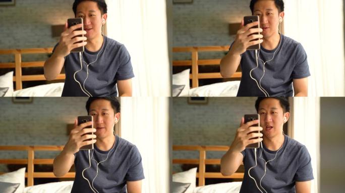 一个快乐的30多岁的亚洲男人穿着休闲服装在家用智能手机进行视频通话。他在电话屏幕上向人们挥手。