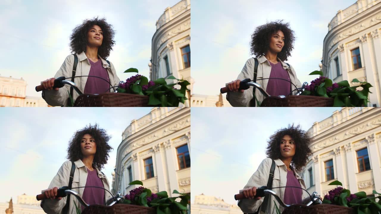 美国黑人模特，卷发，穿着休闲装。微笑着，环顾四周，用车把握着自行车，被建筑物包围着