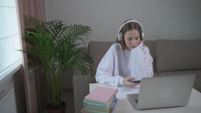 女孩用无线耳机听音乐。桌子上有一台笔记本电脑