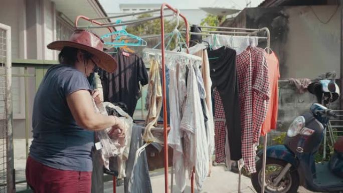 亚洲老女人把衣服从洗衣机上拿下来。在她家门前的衣服晾干。