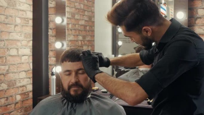 年轻的理发师在理发店为大胡子的男性客户剪头发
