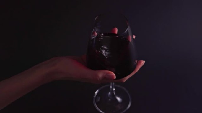 酒味-女人的手在黑色背景上旋转玻璃。酒吧或餐厅的专业人士品尝酒精饮料4k