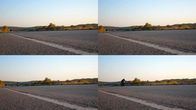 年轻人在空旷的高速公路上快速骑摩托车。摩托车手沿着乡村柏油路高速行驶。喜欢速度的家伙。低角度视图慢动