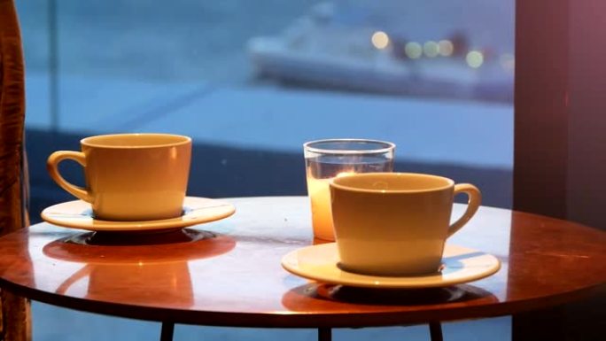 咖啡馆桌上的两个咖啡杯和蜡烛，背景是漂浮的船