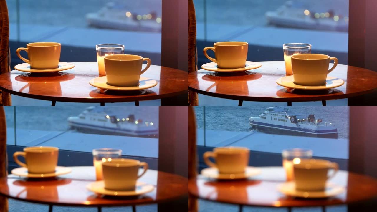 咖啡馆桌上的两个咖啡杯和蜡烛，背景是漂浮的船