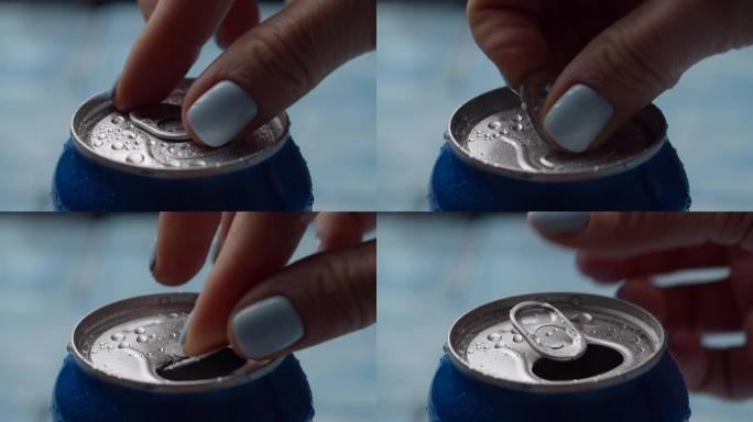 女性手在慢动作的明亮背景上打开湿蓝色汽水罐的特写。蓝色可乐可以打开。