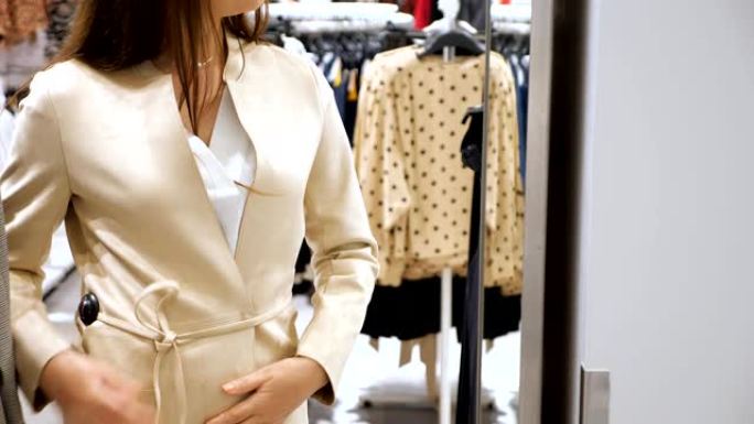 年轻女子在商店的镜子前试穿薄带的奶油色夹克