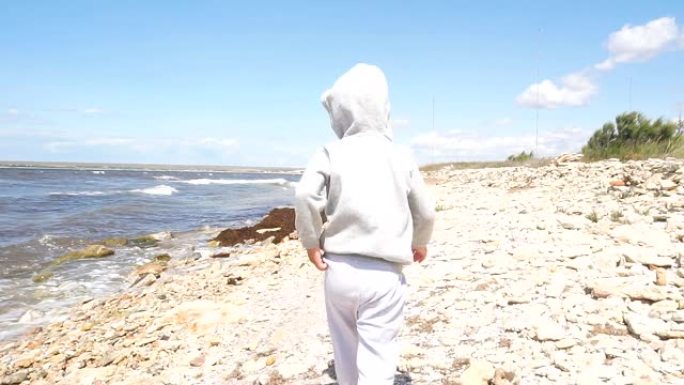 4岁小男孩在多风的天气里走在岩石海滩上