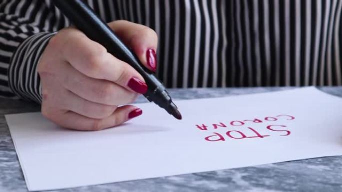 中间是一张纸，一只女性的手在上面写了一个停止冠状病毒，白纸上有一个红色标记，显示了它在相机上的特写。