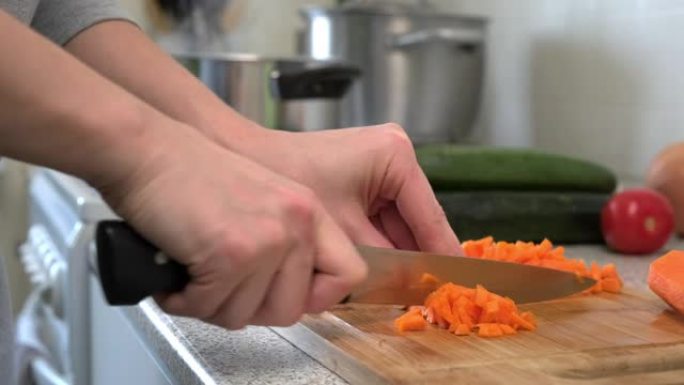 一位女性厨师将胡萝卜切成薄片放在切菜板上做汤。在家做饭。