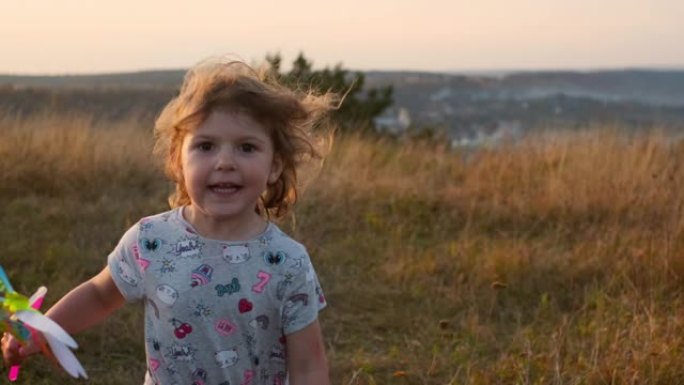在田野里奔跑的可爱的小女孩。她手里拿着玩具风车，随风旋转。