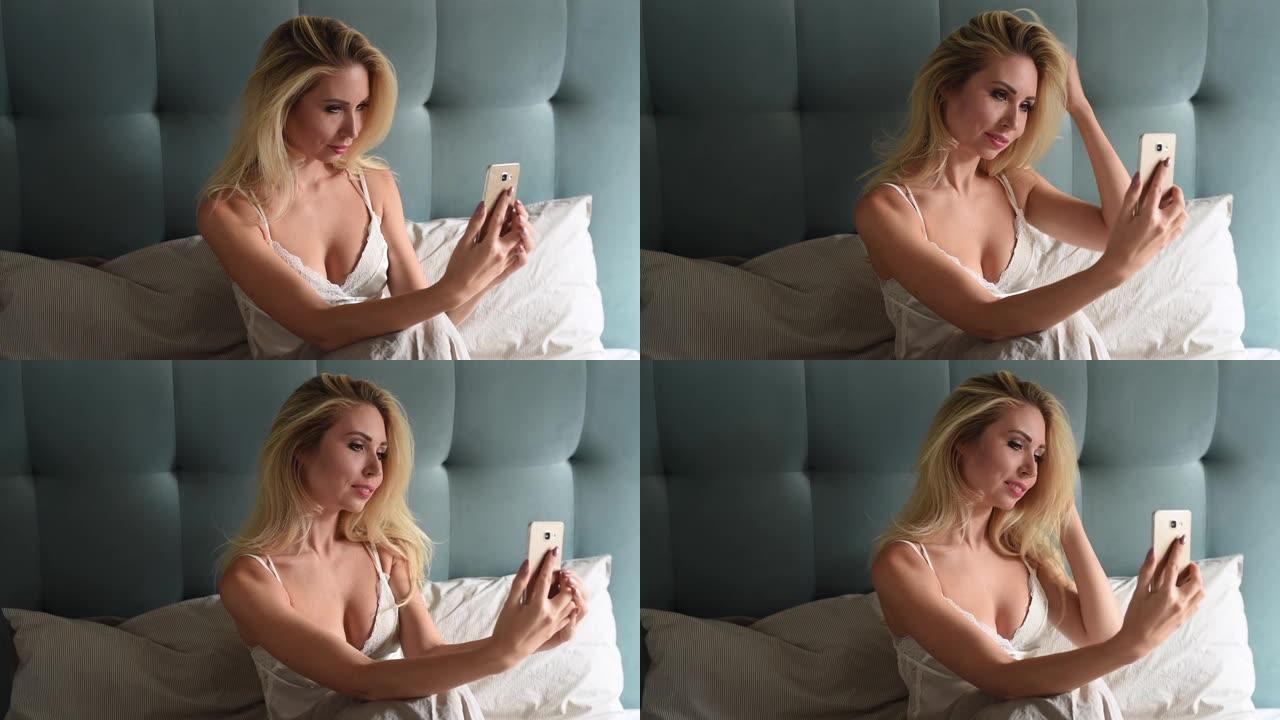 微笑开朗的女人坐在床上放松使用智能手机自拍