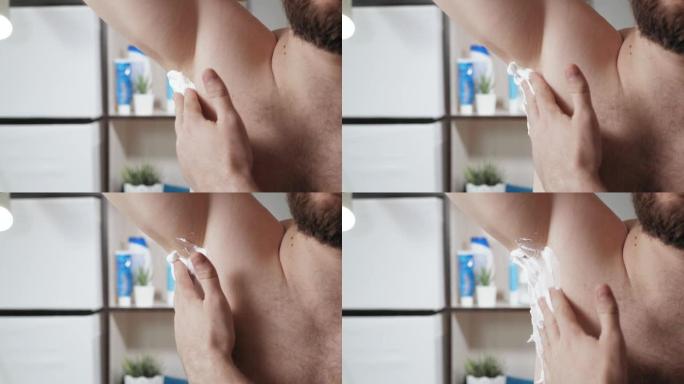 腋下剃须概念。大胡子的白人男子在浴室里用泡沫在右腋下刮胡子。特写