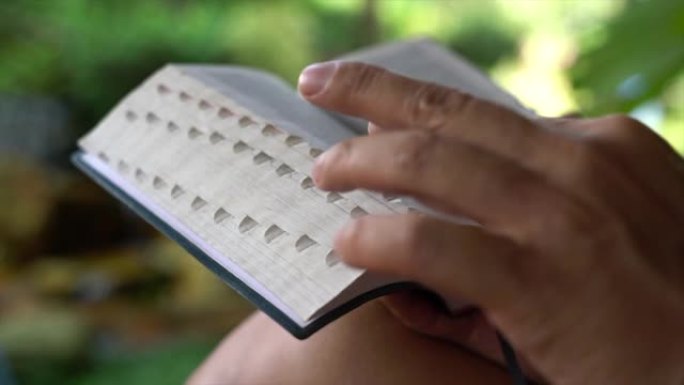 阅读圣经。男人用手指翻页。花园景观。特写。