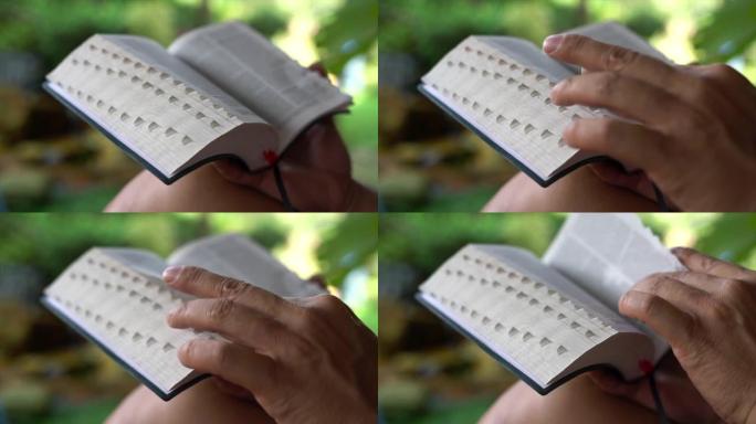 阅读圣经。男人用手指翻页。花园景观。特写。