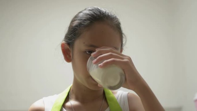 穿着围裙的肖像健康可爱女孩在家里喝一杯牛奶，用舌头舔她的嘴。