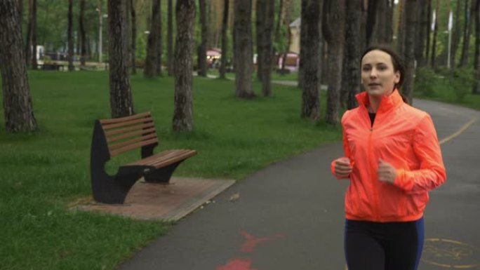 在城市公园慢跑的女跑步者。雨天独自在公园进行健身女性训练。体育运动员早上在林地的休闲区锻炼。健康的生