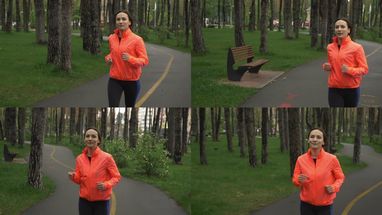 在城市公园慢跑的女跑步者。雨天独自在公园进行健身女性训练。体育运动员早上在林地的休闲区锻炼。健康的生