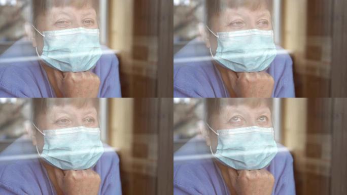 一位戴着医用口罩的老妇看着窗外。检疫自我隔离，冠状病毒，covid 19。