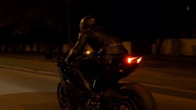 摩托车手在夜城赛车。在小镇的夜间街道上骑着现代运动摩托车的人。旅途中开车的人。自由和冒险的概念。后视