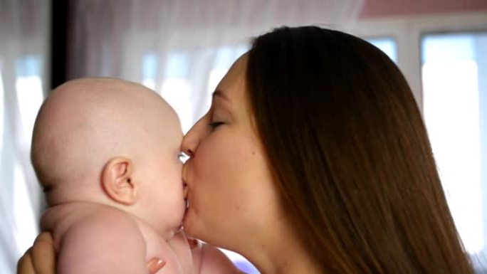 母亲和婴儿。快乐的年轻母亲在家里拥抱婴儿，亲吻胖乎乎的脸颊。特写镜头。