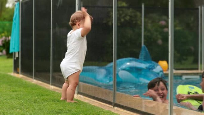 婴儿在苏美日看着孩子们在游泳池水中玩耍。婴儿靠在游泳池围栏上