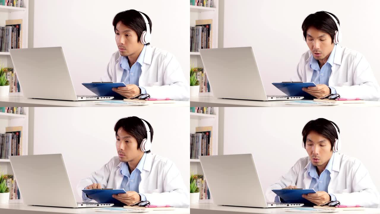 亚洲男性医生戴耳机看报告与笔记本电脑通过视频通话