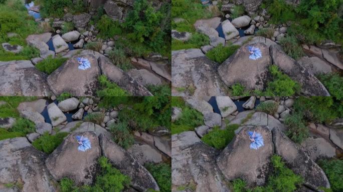 空中: 穿着蓝色连衣裙的漂亮女孩躺在石头上摆姿势。从上方观看。