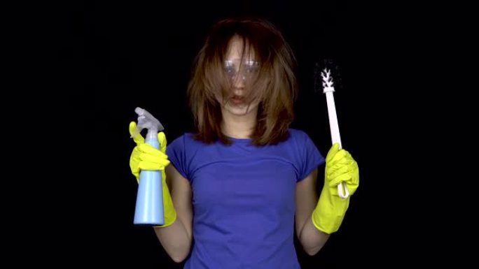 一位头发蓬乱的年轻女子完成了清洁工作。戴着安全眼镜和手套的女人，戴着清洁厕所的工具。女孩拿着马桶刷和