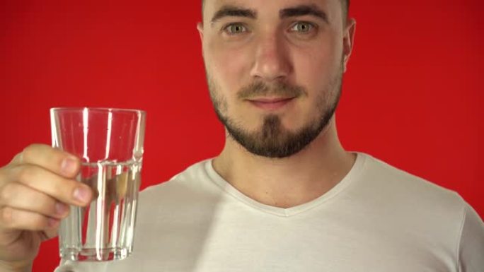 穿着白色t恤的特写有魅力的男人手里拿着一杯水，在红色背景上展示了一个超级标志。健康的生活方式理念。高