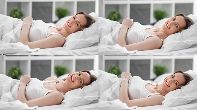 迷人的年轻女性躺在舒适的床上享受早晨。4k龙红相机