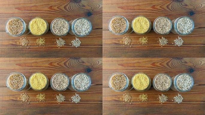 木制背景4k视频玻璃罐中的谷物。收集不同的粒顶视图大麦，燕麦，小米和小麦。全麦食品高纤维含量平铺。健