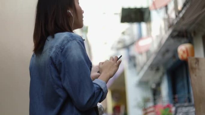 迷人的亚洲女性使用智能手机在泰国曼谷的一条小街道上寻找地图，享受东南亚暑假旅行假期。