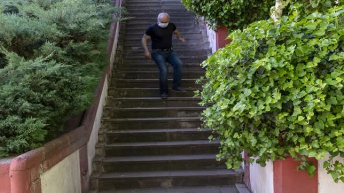 时间流逝-活跃的高级男子在宵禁自由日在公园的楼梯上戴着面具跳跃，在冠状病毒时期的宵禁中安卡拉