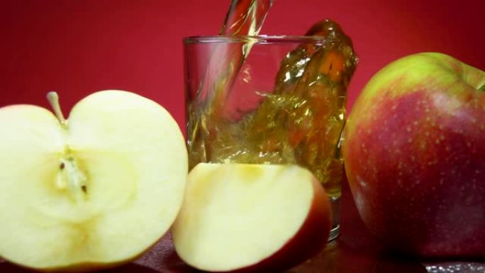 将苹果汁倒入红色背景上成熟的苹果旁边的玻璃杯中