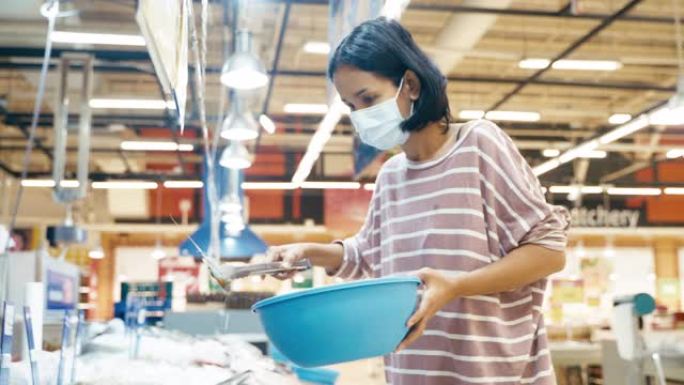 年轻的亚洲妇女选择虾和海鲜冷冻在超市商店的冰与面罩保护从电晕病毒或COVID19和流感健康。