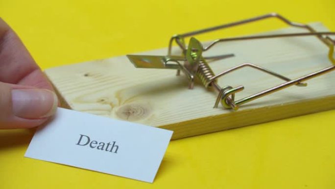 捕鼠器在黄色背景上，一只女性的手在她旁边放了一张纸条，上面写着 “死亡”。不良生活方式陷阱概念。