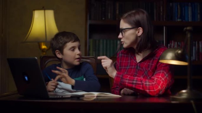 男生在家和30多岁的年轻母亲做在线作业。孩子看着笔记本电脑，在笔记本上写下来。在家中的在线教育过程。