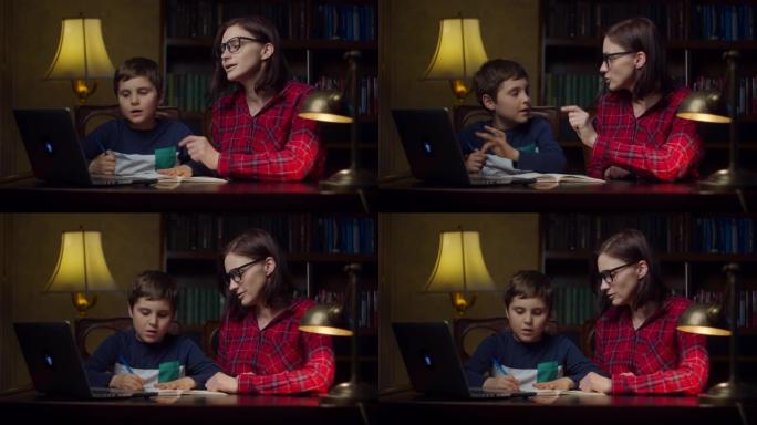 男生在家和30多岁的年轻母亲做在线作业。孩子看着笔记本电脑，在笔记本上写下来。在家中的在线教育过程。