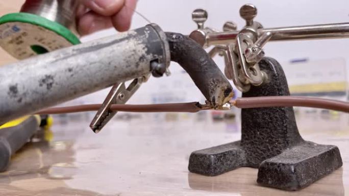 工匠手工焊接两根电线的特写镜头。车间的焊接过程。