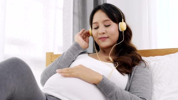 潘拍快乐亚洲孕妇在家卧室床上坐着听音乐，怀孕，人和产妇概念，慢动作