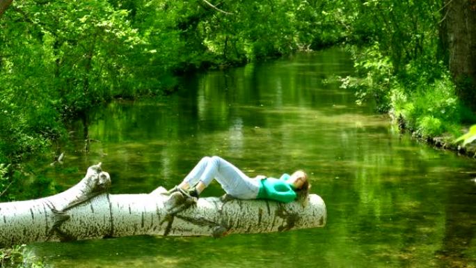 年轻女子独自在森林河上的原木上休息