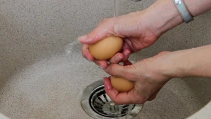女性双手在流动的自来水下清洗生蛋壳