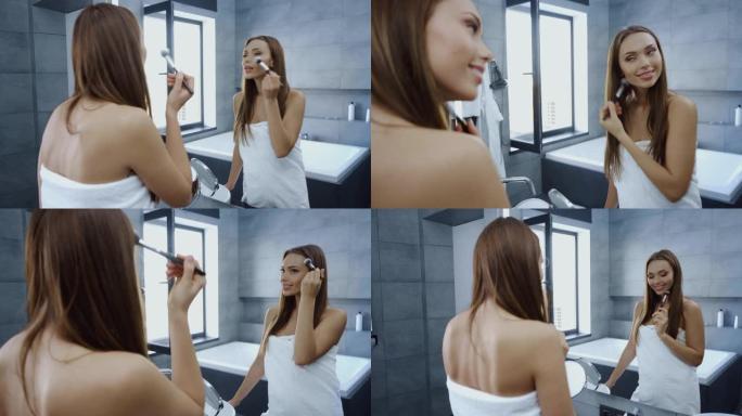 浴巾中的美丽年轻女子在镜子前使用化妆刷