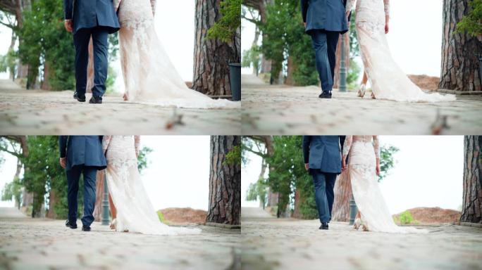 在公园的鹅卵石上伸展着令人惊叹的奶色蕾丝婚纱的特写镜头。婚礼结束后，刚刚结婚的夫妇在花园里慢慢散步。