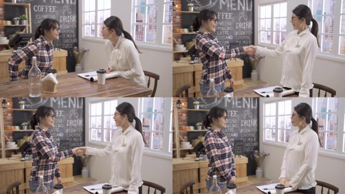 在咖啡店开会时，激动的微笑的亚洲女性申请人与面试官握手。成功的候选人被录用后，面试测试人员说话后站起